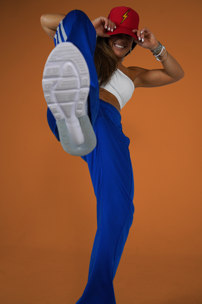 The coach is posing kicking in the air while wearing a blue pants.